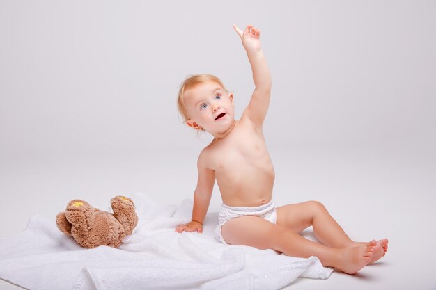 Bambina in pannolino che gioca con l'orsacchiotto su sfondo bianco