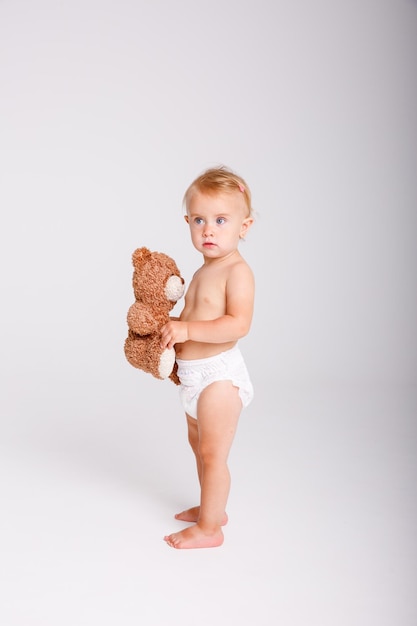 Bambina in pannolino che tiene Teddy bear su sfondo bianco