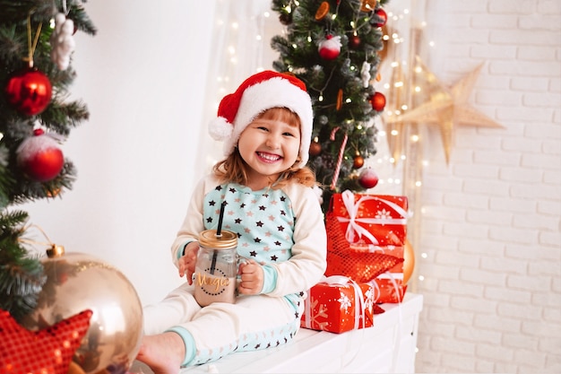 Bambina in pigiama e cappello della Santa che beve latte di cacao