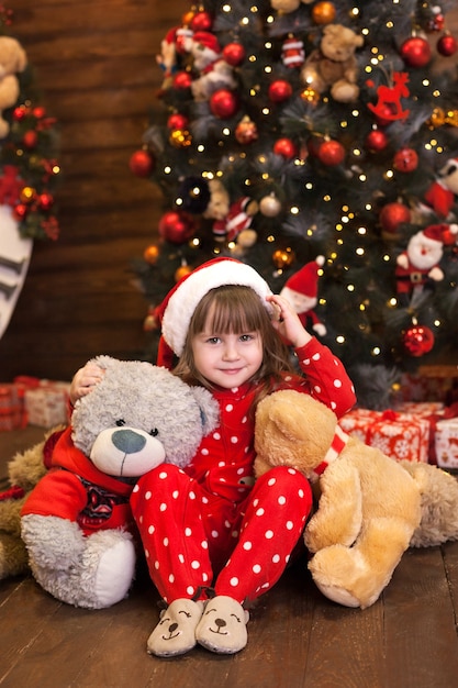 Bambina in pigiama rosso che si siede con i regali dall'albero di Natale