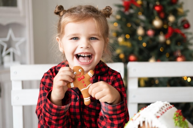 bambina in pigiama rosso che tiene il biscotto degli uomini di pan di zenzero di Natale decorato