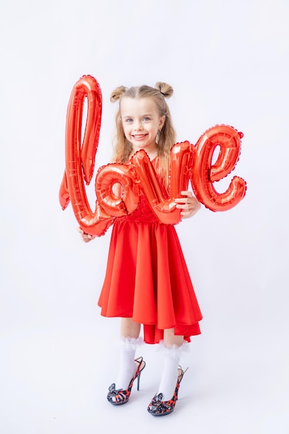 Bambina in pigiama rosso grande palloncino farik con la scritta Love su uno sfondo di legno marrone scuro con cuori rossi il concetto di San Valentino