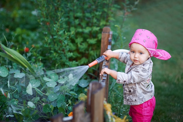 Bambina in stivali rosa che innaffia i fiori