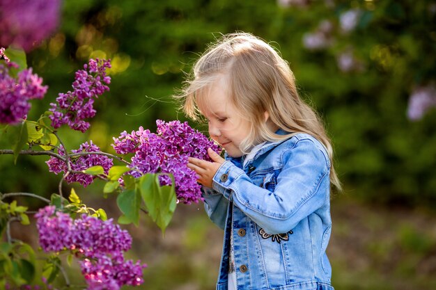 bambina in un abito di jeans cammina nel giardino lilla in primavera