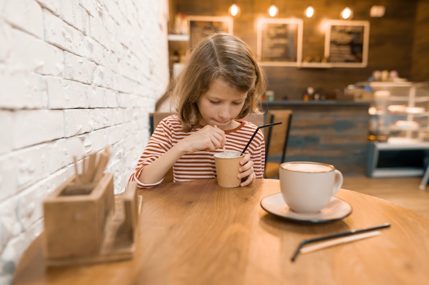 Bambina in un caffè con una bevanda a base di latte