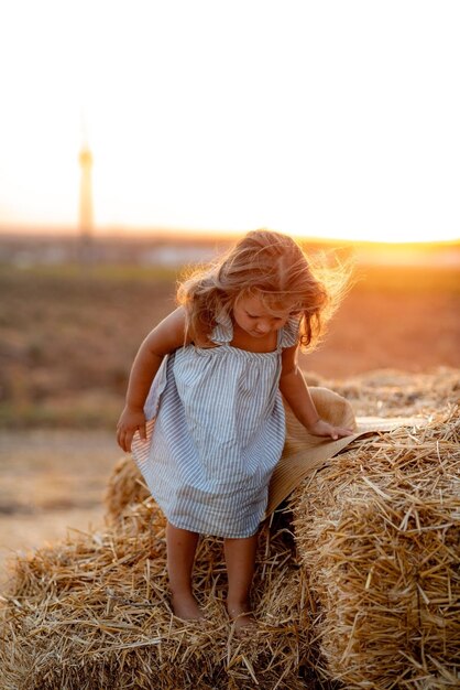 Bambina in un campo con rotoli di fieno al tramonto Paesaggio di un campo con pagliai di paglia al tramonto Una bambina con un vestito blu sta in mezzo a un prato Armonia e amore per la natura