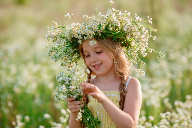 bambina in un campo con una corona che tiene un mazzo di sorrisi di fiori selvatici