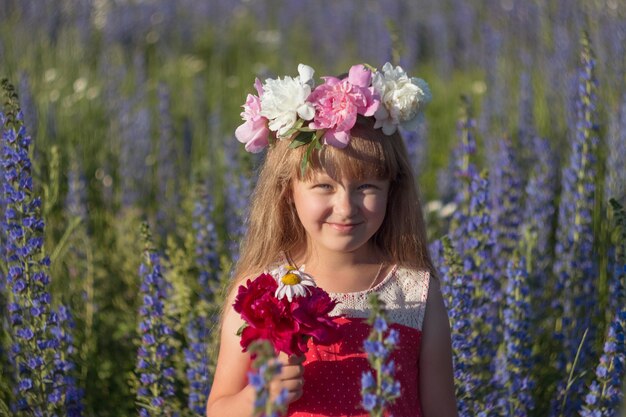 Bambina in un campo di fiori in una soleggiata giornata estiva durante le vacanze estive. Una ragazza con i capelli lunghi sorride.