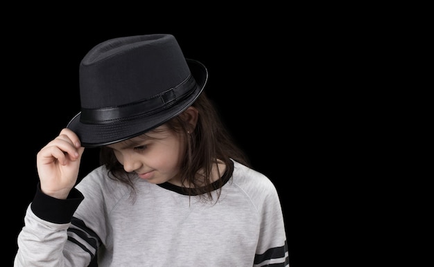 Bambina in un cappello a tesa su sfondo nero.