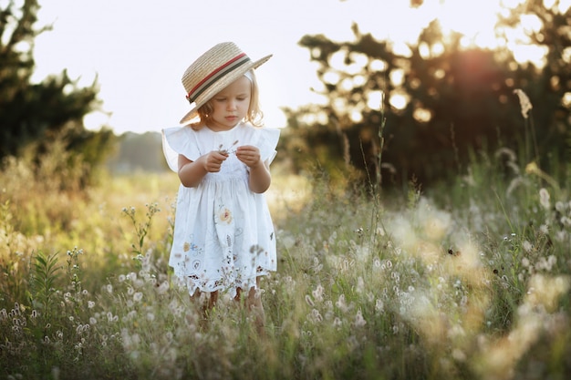 Bambina in un cappello estivo sulla passeggiata al tramonto