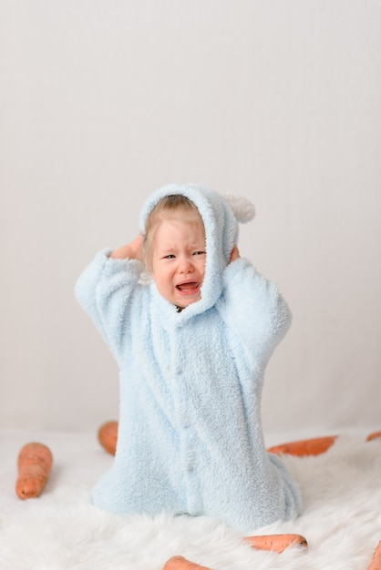 Bambina in un costume da coniglio che mangia le carote.