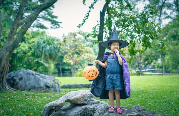 Bambina in un costume da strega che tiene una lampada in halloween