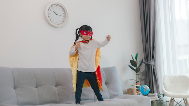 Bambina in un costume da super eroe con maschera e mantello rosso a casa