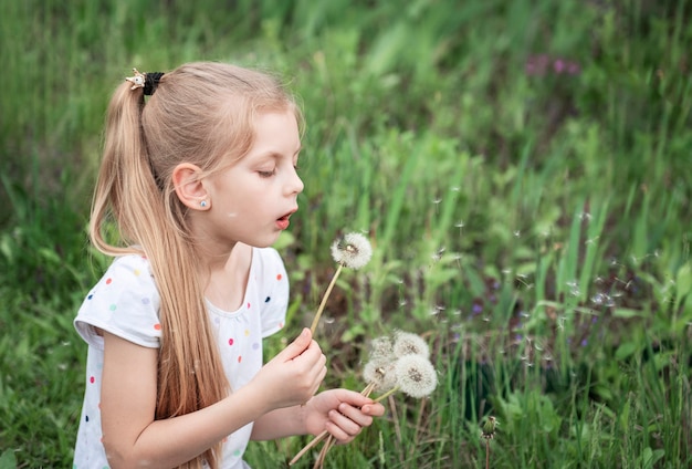 Bambina in un giardino primaverile con denti di leone bianchi nelle sue mani