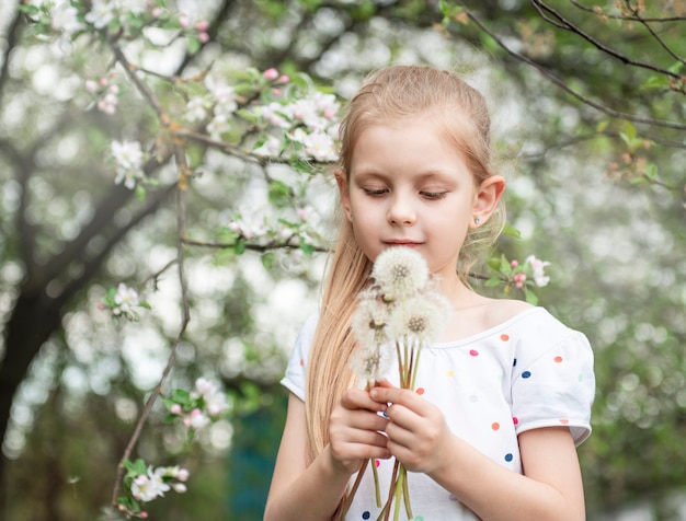 Bambina in un giardino primaverile con denti di leone bianchi nelle sue mani