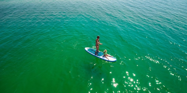 Bambina in un giubbotto di salvataggio seduto sul paddle board con la madre