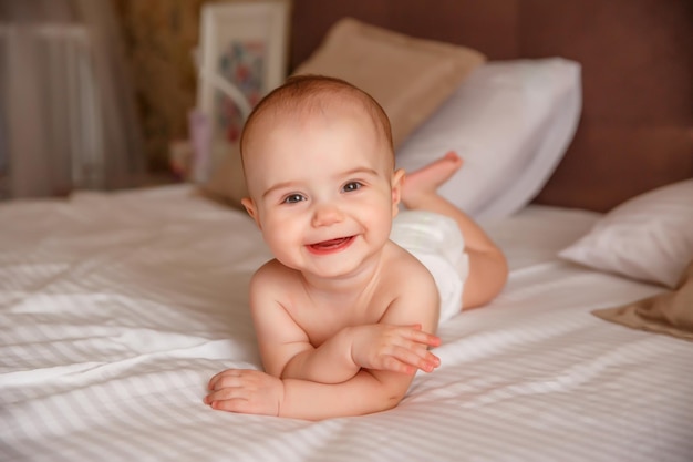 bambina in un pannolino è sdraiata sul letto in camera da letto a pancia in giù sorridente