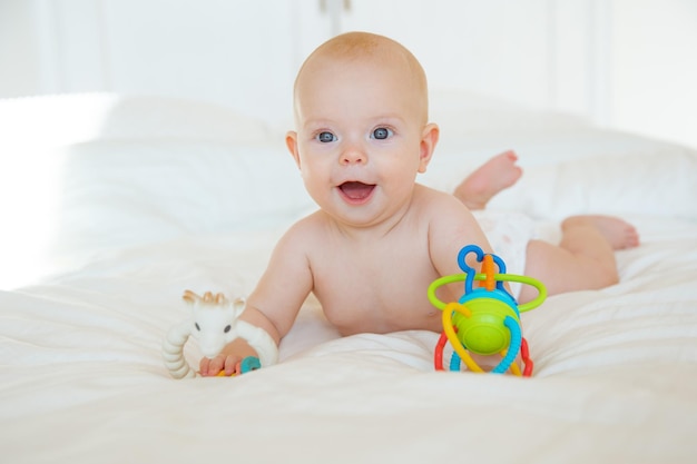 Bambina in un pannolino sdraiato sul letto con sonagli di giocattoli