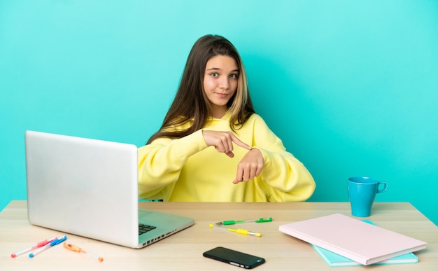 Bambina in un tavolo con un computer portatile su sfondo blu isolato che fa il gesto di essere in ritardo