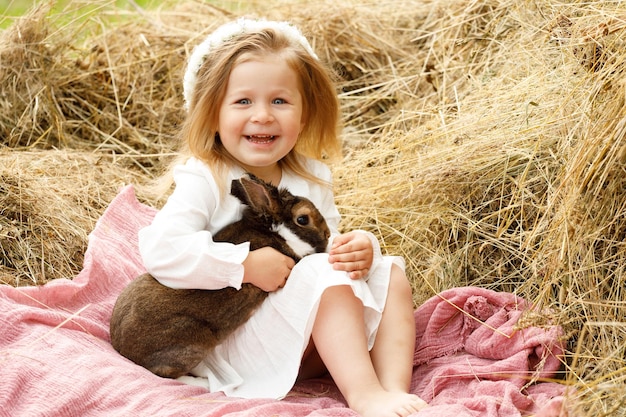 Bambina in un vestito bianco sul fieno con un coniglio