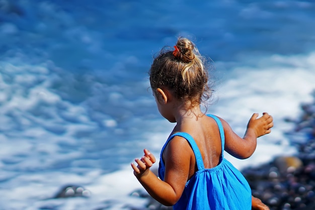 Bambina in un vestito blu che gioca sulla spiaggia di Paradisos in Santorini