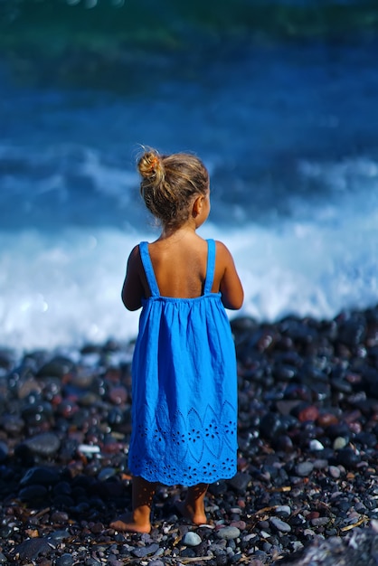 Bambina in un vestito blu che gioca sulla spiaggia Paradisos a Santorini