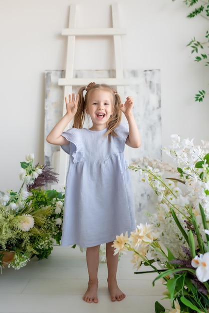 Bambina in un vestito blu è circondata da bellissimi fiori Sorridendo guardando la telecamera e agitando i prodotti Children39s