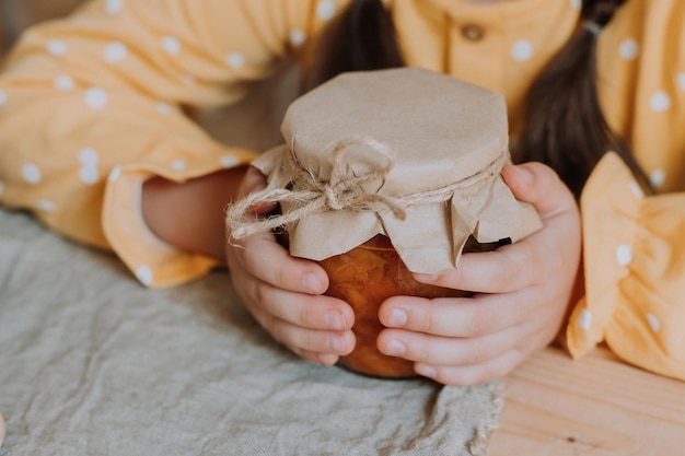 bambina in un vestito giallo con una spatola di legno in mano e marmellata in un barattolo di vetro in cucina