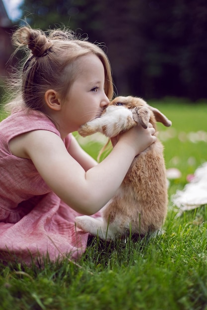 Bambina in un vestito rosa bacio coniglio in un prato verde in estate Divertente amicizia tra un bambino e un animale durante la Pasqua