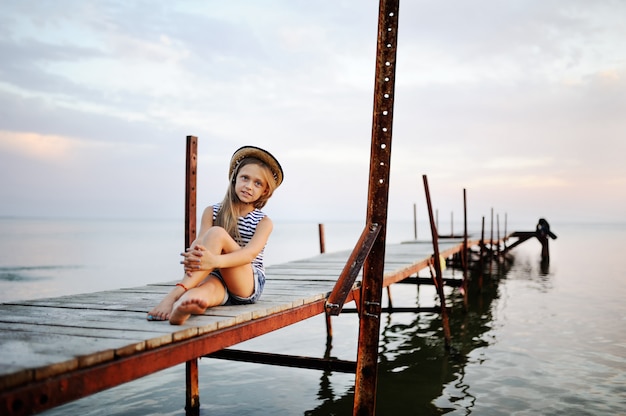 Bambina in una maglietta a strisce che si siede sul ponte del mare