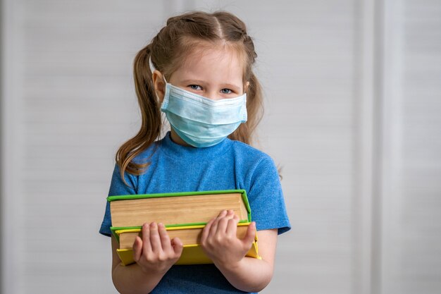 Bambina in una mascherina medica con un libro in sue mani