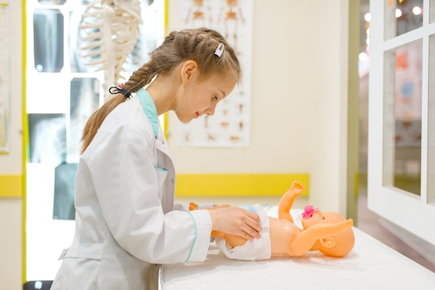 Bambina in uniforme che gioca medico con la bambola del giocattolo