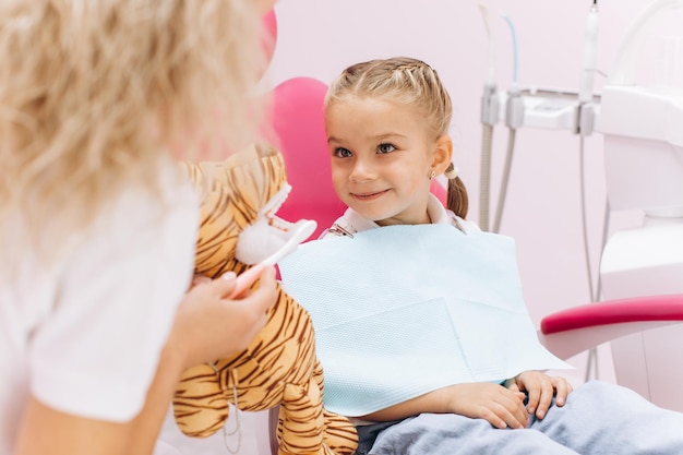 Bambina in visita dal dentista che tiene un giocattolo e mostra come lavarsi i denti in una clinica dentale