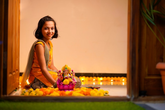 Bambina indiana carina che fa decorazioni con fiori e lampada a olio per il festival di diwali a casa.