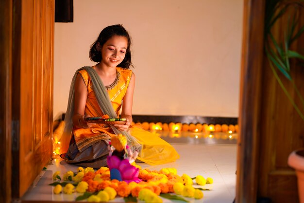 Bambina indiana carina che fa decorazioni con fiori e lampada a olio per il festival di diwali a casa.