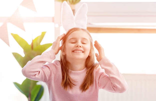 Bambina indossa orecchie da coniglio sorridente nella stanza soleggiata al giorno di Pasqua