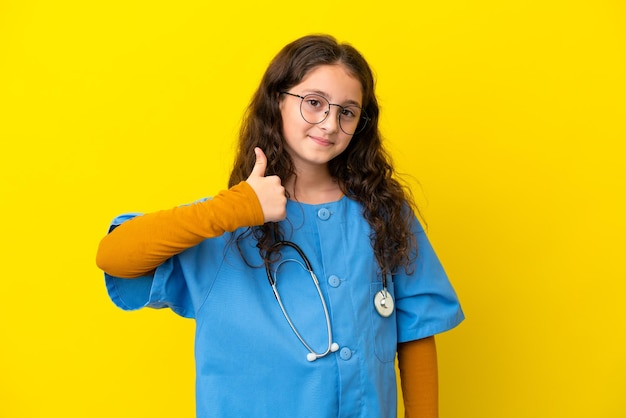 Bambina infermiera isolata su sfondo giallo con i pollici in su perché è successo qualcosa di buono