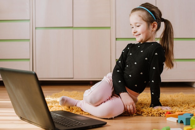 Bambina intelligente che gioca con il computer portatile nella sala giochi a casa