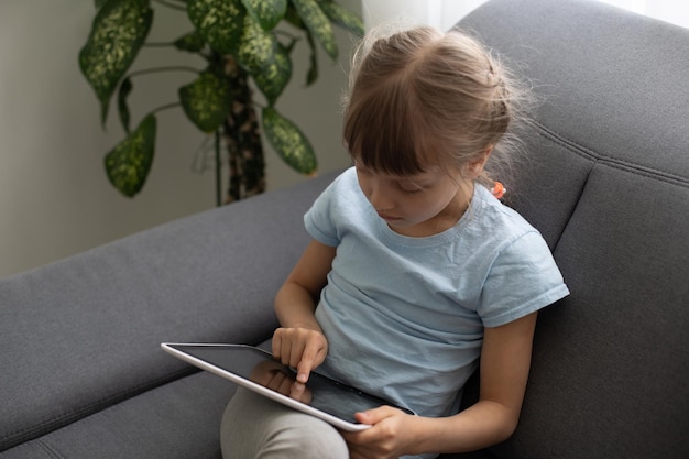 Bambina intelligente che utilizza un computer tablet mentre è seduto sul divano nel soggiorno di casa.