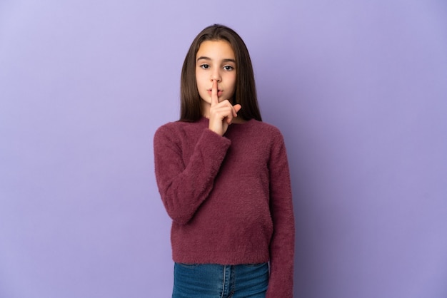 Bambina isolata sulla porpora che mostra un segno del gesto di silenzio che mette il dito in bocca