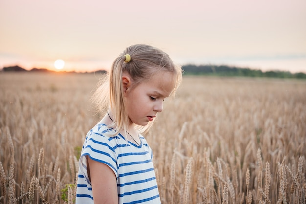 Bambina nel campo di grano giallo al tramonto del paesaggio estivo, sfondo agricolo estivo con picchi di grano maturo