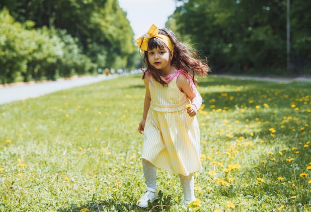 Bambina nel parco che raccoglie fiori gialli di tarassaco in una soleggiata giornata estiva