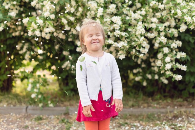 Bambina nel parco in una giornata di sole Todler ragazza in giardino sotto l'albero in fiore Pioggia di petali di primavera Concetto di primavera felice infanzia pace nel mondo pace e felicità armonia