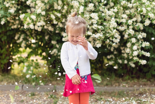 Bambina nel parco in una giornata di sole Todler ragazza in giardino sotto l'albero in fiore Pioggia di petali di primavera Concetto di primavera felice infanzia pace nel mondo pace e felicità armonia