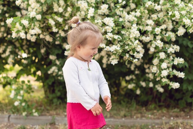 Bambina nel parco in una giornata di sole Todler ragazza in giardino sotto l'albero in fiore Pioggia di petali di primavera Concetto di primavera felice infanzia pace nel mondo pace e felicità armonia