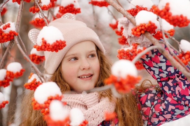 Bambina nella neve da un ramo di sorbo. Concetto sano.