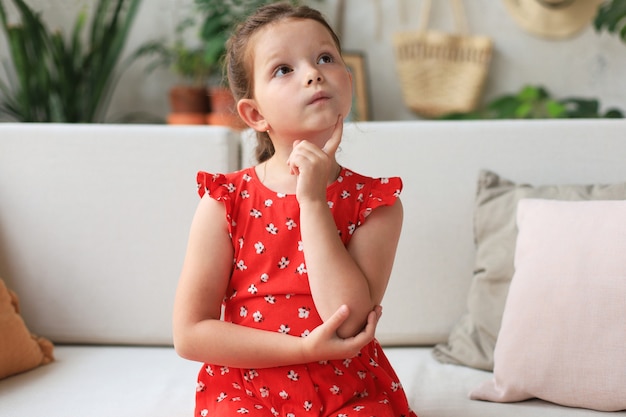 Bambina pensierosa che si siede sul divano in soggiorno. Sognare ad occhi aperti.