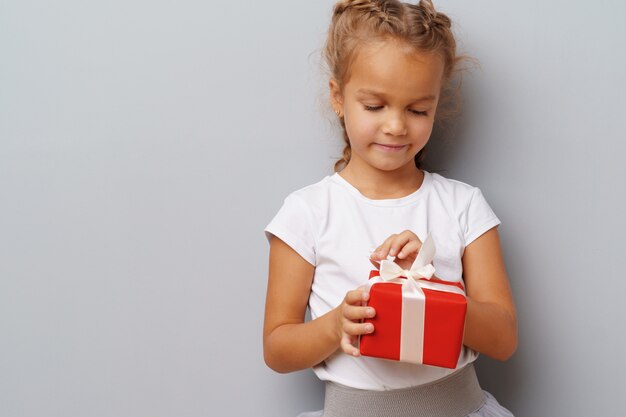 Bambina piacevole che tiene un contenitore di regalo rosso in sue mani