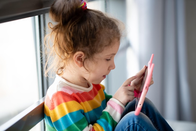 Bambina positiva che tiene in mano il computer tablet Pubblicità di una nuova app educativa per gadget