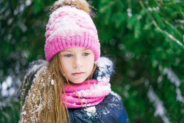 Bambina premurosa con cappello rosa nella foresta invernale